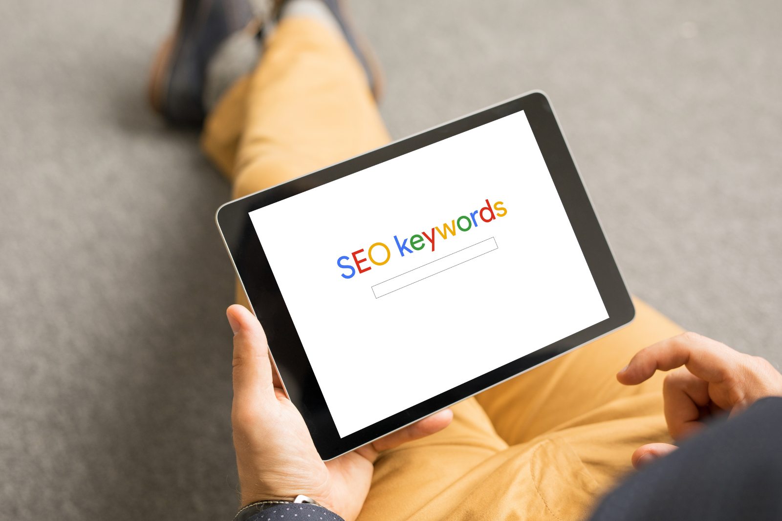 Man holding a tablet that says "SEO Keywords" in the same font as Google's logo